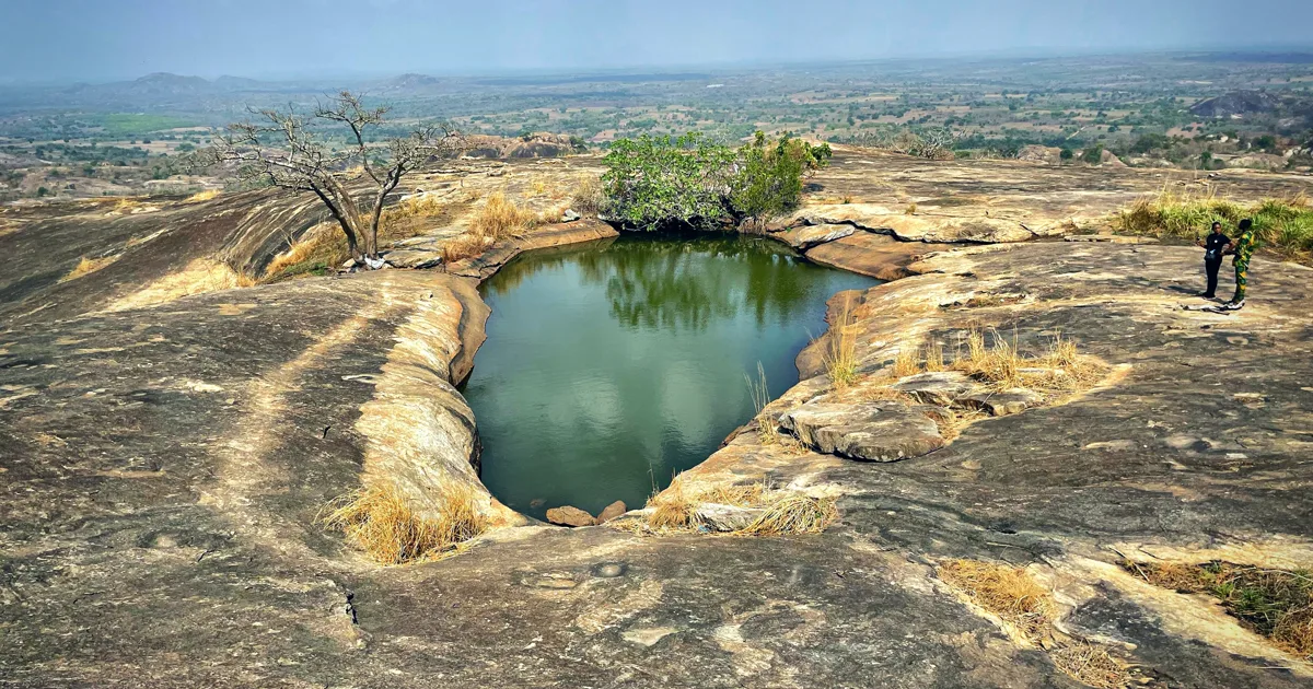 Visitors standing beside Iyake Suspended Lake on the rocky summit of Ado-Awaye Mountain in Oyo State.