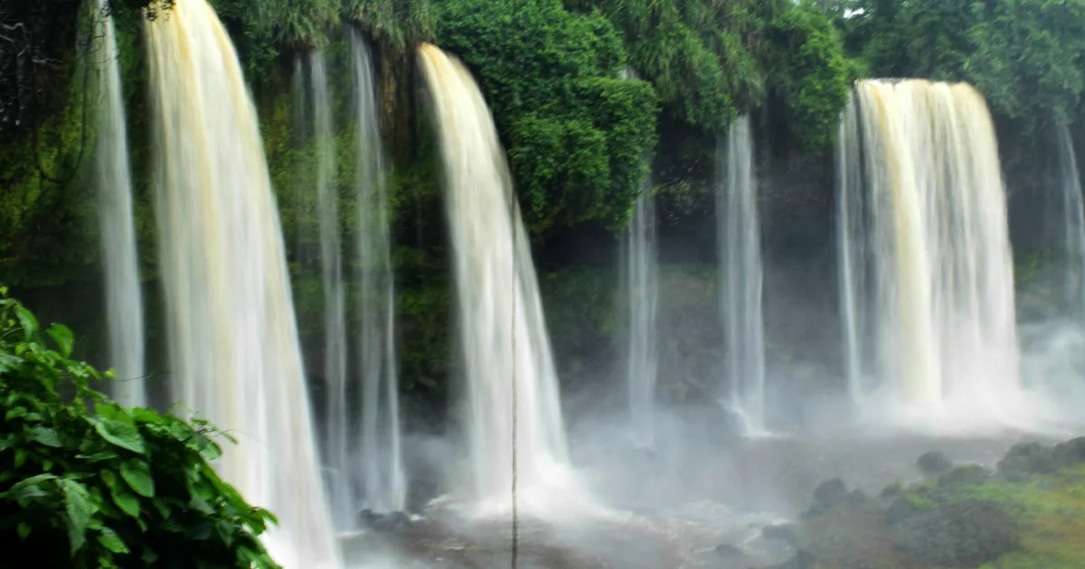Several streams cascading together over a wide rainforest cliff at Agbokim Waterfalls in Cross River State.