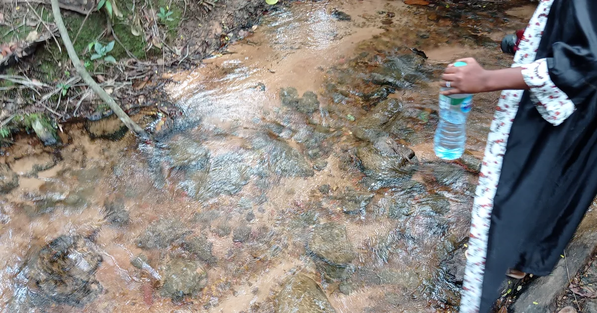 A visitor walking beside the rocky stream leading towards Awhum Waterfall and Cave in Enugu State.