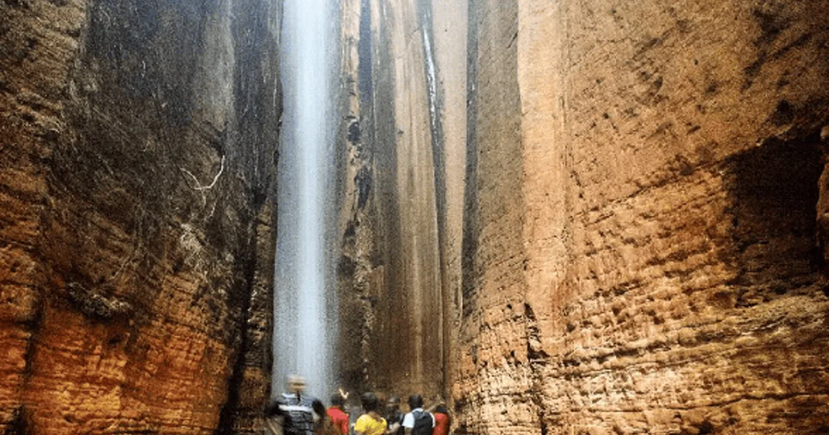 Visitors standing beneath the narrow waterfall dropping through an opening inside Ngwo Cave in Enugu.