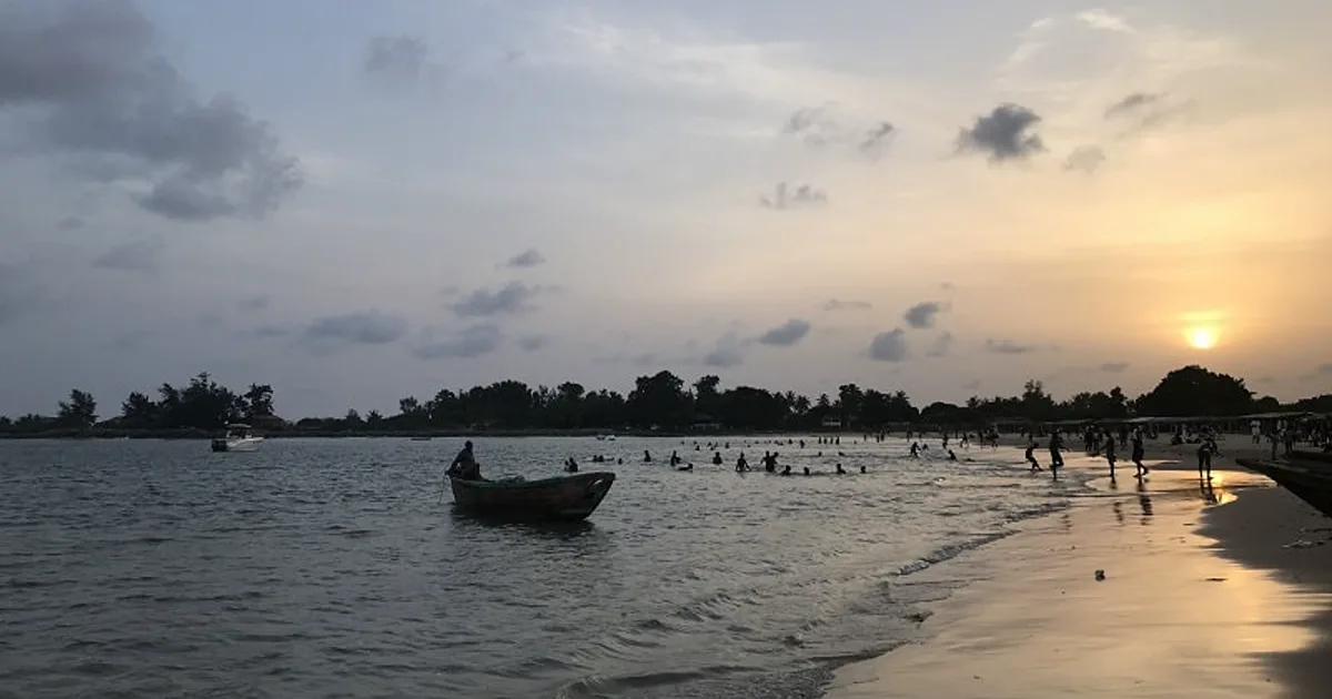 A passenger boat crossing the water as visitors enjoy Tarkwa Bay Beach in Lagos at sunset.