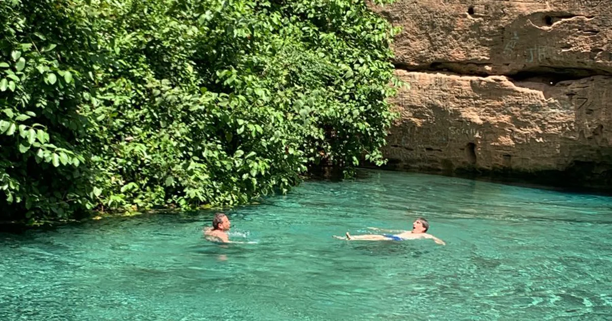 Two visitors swimming in the clear turquoise water of Wikki Warm Spring at Yankari Game Reserve.